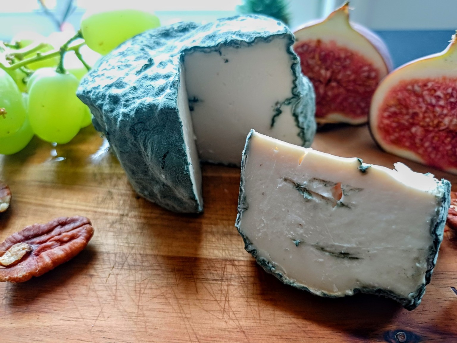 A wheel and wedge of Vegan-Lee blue cheese served with grapes, figs and pecans